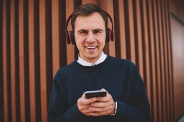 Yarım uzunlukta boş vakit yaz Street ve modern teknoloji kullanılarak yakışıklı neşeli erkek öğrenci portresi. Mutlu adam kulaklıklar ile en sevdiğiniz müzik dinlerken eğleniyor