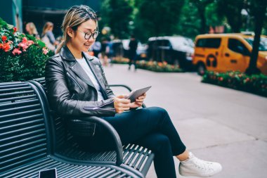 Açık havada elektronik gönüllülük dinlenme Asya kız öğrencinin kitap kentsel ayarları, video oturma n tezgah tablet ve kablosuz internet kullanarak şehir izlerken olumlu Çinli kız genç gülümseyen