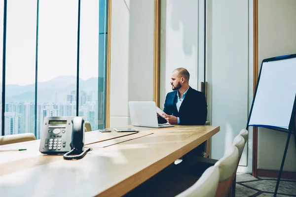 认真的商人 有会计报告的手坐在笔记本电脑在自己的办公室 而看着窗外 自信的公司董事在现代上网本的会议桌上工作 — 图库照片