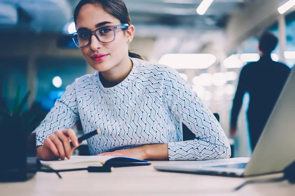 眼镜制作中的熟练女员工肖像创建报告坐在桌面上的现代笔记本电脑 沉思的女人看相机分析信息 在工作地点启动 — 图库照片