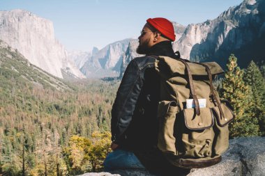 Genç hipster adam vahşi doğanın nefes kesen sahne zevk keşfetmek Yosemite Milli Parkı, yüksek rock cliff seyir orman Vadisi üzerinde üzerinde bakış açısı dinlenme sırt çantası ile erkek gezgin
