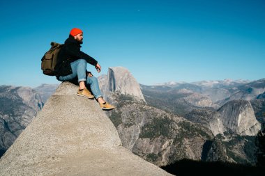 Hipster herifin Dağı'na üzerinde yolculuk tutkusu macera zevk abys aktif, hafta sonları harcama doğanın nefes kesen sahne seyir üzerinde yüksek kayalık uçurum üzerinde oturan genç erkek gezgin