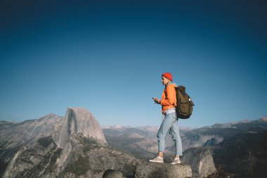 Hippi kız rock cliff nefes kesen manzarası ile iyi bir bağlantı almak hiking, yalnız kadın yolculuk tutkusu tarihinde temasta smartphone kullanarak üzerinde ayakta keşfetmek mobil şebeke kapsama dağ vahşi doğa