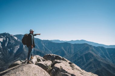 Dağda işaret sırt çantası ile genç erkek seyahat Tur, hil mesafeden konumu gösteren Milli Parkı manzara keşfetmek adam yolculuk tutkusu hiking sırasında rock cliff üzerinde duran doruklarına