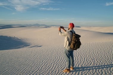 Resim doğal ufuk cep telefonunuzun gezisi, Erkek gezgin çöl nefes kesen Panoraması zevk Smartphone'da video çekim sırasında dunes üzerinde yapım sırt çantası ile hipster adamın arkadan görünüm