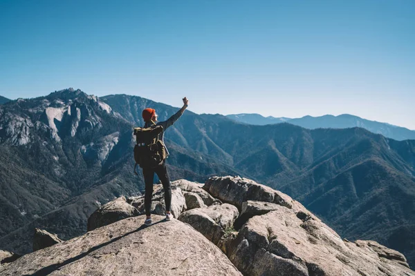 年轻女性探险家与旅游背包制作自拍在山上的岩石悬崖上的智能手机相机 时髦的女孩流浪徒步旅行拍摄 Bloggin 细胞的图片 — 图库照片
