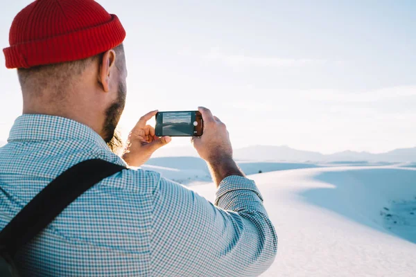 Back view of male traveler taking picture of beautiful desert scenery landscape on cellular during journey, guy wanderlust using smartphone camera for making image of breathtaking White sands nature