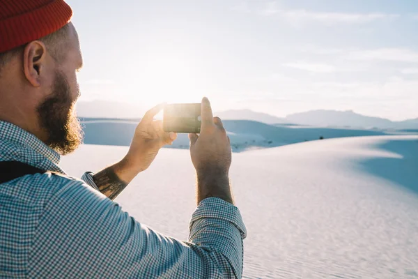 裁剪图像的家伙流浪拍照片的沙漠沙丘景观在智能手机相机在旅行期间 关闭了男性旅行者在白色沙滩上拍摄视频通过应用电话为 Bloggin — 图库照片