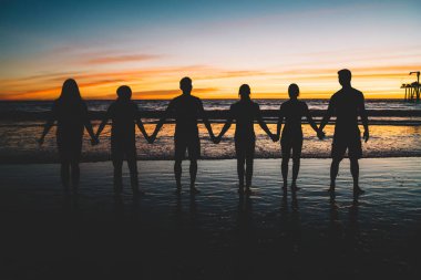 Grup birlikte deniz sahne günbatımında sırasında yaz tatillerini, siluet tatil zevk arkadaş ayakta el ele tutuşarak genç erkek ve dişi kişi. Mutluluk, topluluk, dostluk