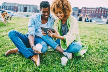 Mutlu koyu tenli hipsters sosyal ağlara yükleme ortak resimler parkta birlikte, istirahat ederken gülümseyen kıvırcık saç video izlemek ile siyah kadın erkek taşınabilir PC ile hesap