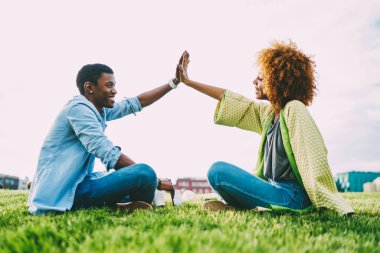 Yüksek beş oturan yeşil çim çim güneşli günde vererek ellerini yükselterek mutlu afro Amerikalı arkadaşlar trendy Şehir Parkı açık havada toplantıda sırasında başarı kutluyor koyu tenli hipsters giyinmiş.