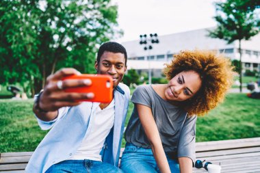 Güzel afro amerikan kız sevgilisini modern smartphone, Çift lovemaking selfie bahar güneşli günde Park'ta dinlenme zevk birlikte kullanarak resimler için poz kıvırcık saçlı