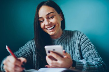 Komik Haberler Üniversitesi'nde oturan, telefon belirterek neşeli genç kadın. Pozitif esmer öğrenci komik video online dijital hücresel izlerken ve metin günlüğüne yazma sonra gülüyor