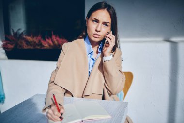 Metin bilgileri Not Defteri'nde belirterek meslektaşım ile smartphone üzerinde konuşurken işkadını. Not defteri açık havada kafede otururken yazma bilgi analiz mobil konuşmayı şık genç kadın