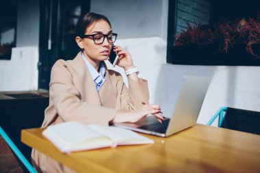 Hippi kız ile smartphone uygulama laptop indirmeye çalışıyor yükleme hatası hakkında konuşurken. Genç kadın gözlük dizüstü bilgisayar mesafe iş sırasında cep üzerinde iletişim