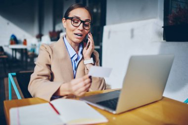 Kartvizit smartphone aygıt açık havada dizüstü bilgisayarda kafede oturan başarılı iş teklifi hakkında telefonla konuşurken elinde tutan gözlük neşeli hippi kız