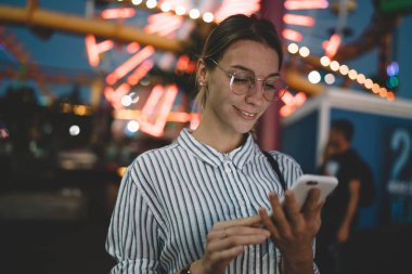 Smartphone akşam eğlence parkı, pozitif kadın turist yapım sonrası cep kullanarak santa monica pier cazibe hakkında sosyal ağ üzerinde yeniden oluşturmak üzerinde gülümseyen hippi kız fotoğrafları 