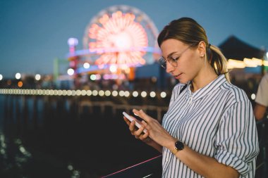 Kadın turist Web sitesinde boş zamanlarında eğlence parkı, hippi kız bloglama sosyal ağ yolu ile cellphone dönme Santa monica pasta plajda akşam harcama smartphone tarama