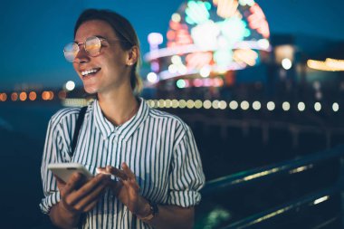 Lunaparkta gece holding smartphone, mutlu hippi kız ile Santa monica pier cellula kullanarak harika hafta sonu heyecanlı dinlenme arkadaş mesaj komik neşeli kadın turist