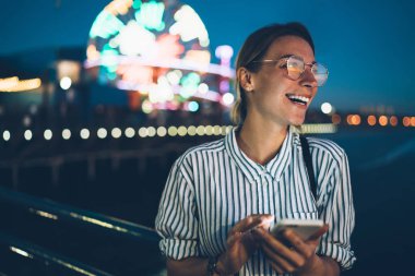 Santa monica pier seyahatini gece holding smartphone, bloglama ünlü turistik showplace yeniden oluşturmak için cep telefonu kullanarak gülerek mutlu hippi kız gülümseyerek başarılı genç kadının