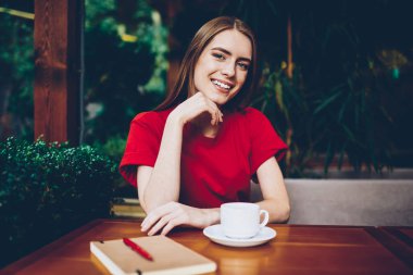 Gülümseyen güzel kadın kamera kafede lezzetli cappucino bardak ile dinlenme bakarak, yarı uzunluk portre. Rekreasyon vaktinizi kafeteryasında olumlu çekici genç kadın