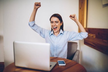 Eller yükselterek ve dizüstü bilgisayar bağlı kablosuz internet şık coworking uzayda oturan oturan Web sitesinde online yarışma kutluyor kazanma çığlık kaygısız hippi kız