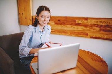 Öğrenci dizüstü bilgisayar coworking içinde oturan internet sitesinden Eğitim Semineri, Not Defteri'nde planı kavramı aşağı yazma. Webinar netbook üzerinde izliyor ve notlar neşeli genç womn