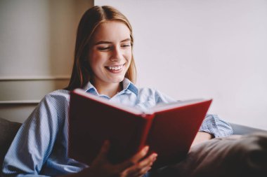 Çekici sarışın saçlı hippi kız komik Arsa yeni bestseller okuma sırasında gülüyor. Koltukta oturan ünlü yazarların favori koleksiyonunun heyecan verici kısa hikaye zevk kitap kadın sevgilisi