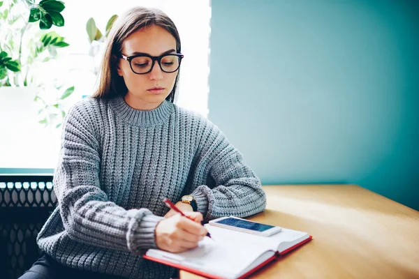 Nachdenkliches Hipstermädchen Optischer Brille Das Checkliste Notizbuch Schreibt Sitzt Holztisch — Stockfoto