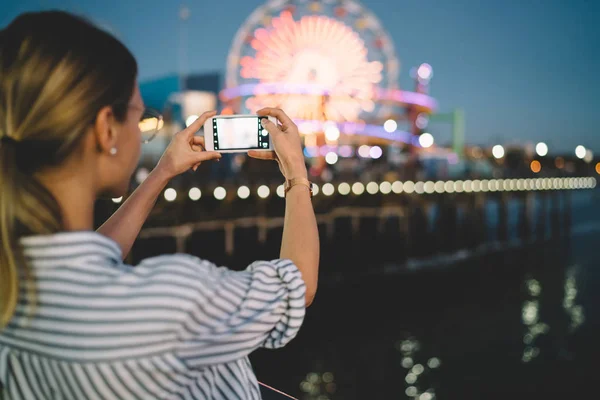 女性游客的背部视图使用智能手机制作闪亮的摩天轮图片在晚上在游乐园 时髦女孩拍摄视频博客上的手机休息在著名的 Showplac — 图库照片