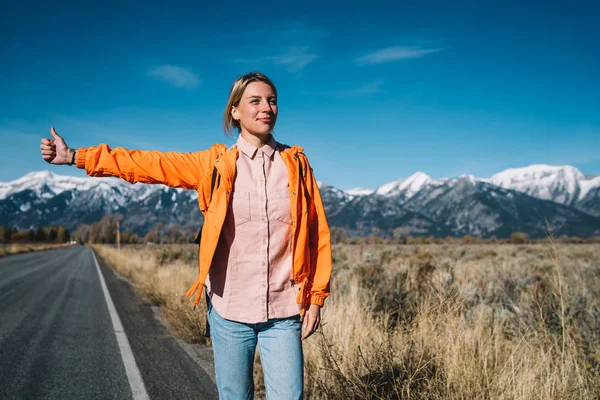 Ulusal oto stop seyahat, kadın yolculuk tutkusu ayakta yaz aylarında doğa otostop keşfetmek için işaret yükselterek karayolu üzerinde gülümseyen Park asfalt yolda araba için bekleyen olumlu hippi kız