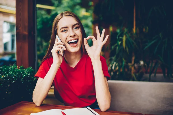 Başarılı iş projesi smartphone telefon görüşmesi sırasında tartışmak ve popüler jest okey yandan kameraya gülümseyen sırasında gösterilen neşeli genç girişimci portresi yarım uzunluk