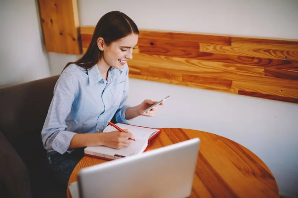 Geschoolde Jonge Vrouw Neerschrijven Van Tekstgegevens Kladblok Vanaf Internetwebsite Telefoon — Stockfoto