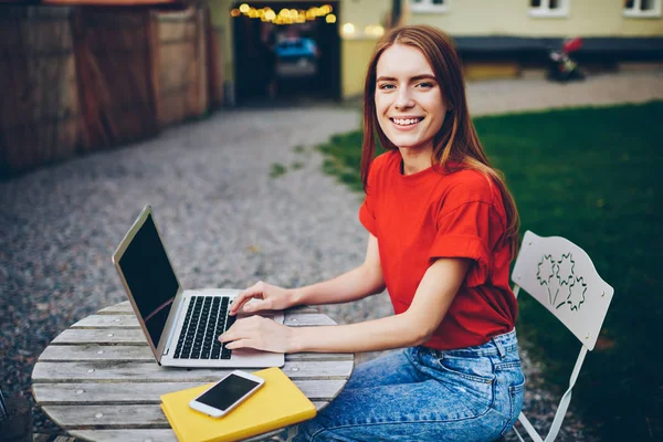 Portrait of cheerful female blogger messaging with followers about last video post on netbook with mock up area for your webpage sitting in urban setting.Positive student typing coursework on laptop