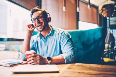 Neşeli sakallı adam 30 yaşında modern Kulaklığımda çalma listesinden en sevdiğin şarkı zevk ve having fun kafede lezzetli kahve reklam için reklam alanı yakınında masada oturan Eyewear