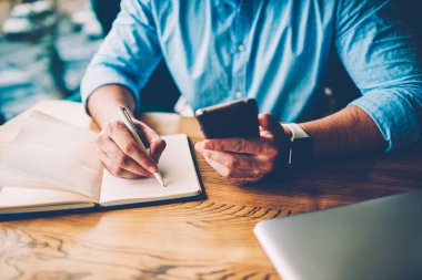 Modern smartphone tutarak ve aşağı kafede farklı web sitelerinde bilgi aramak için yüksek hızlı internet bağlantısı kullanarak bir not defteri kısa mesaj yazma erkek el resim kırpılmış