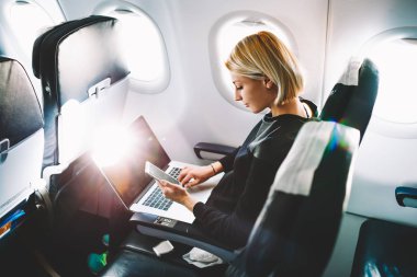 Sarışın kadın turist gelen bildirim netbook ile uçak koltuğunda oturan Smartphone cep telefonu ile kontrol. Genç işkadını paylaşmak medya telefonu dizüstü bilgisayar üzerinde uçak uçuş sırasında
