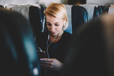 Uçağın modern kulaklık dijital smartphone aygıt gemide kablosuz bağlantı ile memnun ilginç film online izlerken üzerinde uçuş sırasında vakit içinde çekici kadın yolcu