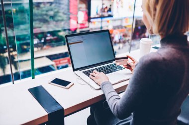 İçinde webstore alışveriş ve kablosuz Internet üzerinden kredi kartı ile online ödeme yapmadan kafede dizüstü bilgisayara bağlıyken dikiz genç kadın kulaklık Web sitesi üzerinden müzik dinleme kırpılmış