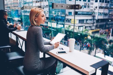 Çekici neşeli genç kadının cityscape kafede oturan boş ekran alanı ile modern tablete kullanma yolu ile ücretsiz 4 g internet bağlantısı kurarken pencereden dışarı bakıyor