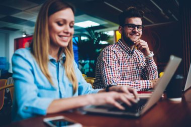 Internet bağlantısı kullanarak ortak proje için kadın meslektaşım web sitelerinde arama bilgi modern dizüstü bilgisayar ile birlikte çalışma sırasında kamera gülümseyen neşeli genç adam portresi