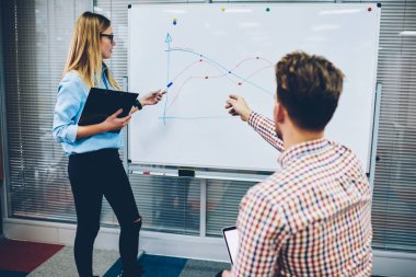 Flipchart diyagramları ve Üniversitesi'nde ders sırasında öğretmen soru cevap ile işaret eden öğrenci. Elinde doğru düzeni yeni grafik açıklayan on board çizilmiş gösteren işaretçisi ile kadın koç