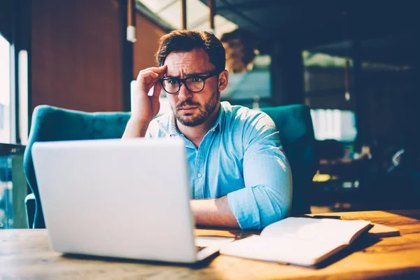 Shocked man in eyeglasses reading strange news in internet sources on modern computer.Astonished businessman watching webinar on laptop connected to wireless 4G internet sitting in stylish coffee shop