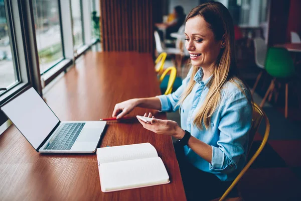 Mutlu kadın freelancer alınan komik bildirim Smartphone cep telefonu ile uzaktan modern netbook boş ekran alanı ile çalışan kablosuz 4 g için bağlıyken Internet alanı coworking oturan