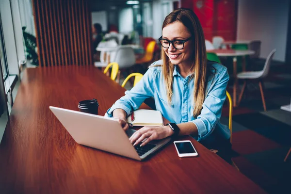 Neşeli hipster öğrenci Eyewear online sosyal ağlar dizüstü bilgisayar üzerinde arkadaşlarıyla sohbet ederken gülüyor vizyon düzeltme için bağlı kablosuz 4 g için internet kafede oturan