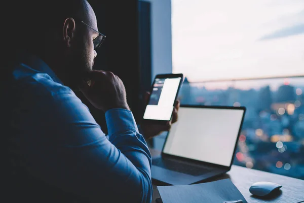 Contemplative male it developer installing new app on tablet with mock up screen working late in office,businessman browsed  web page on portable pc reading network content analyzing information