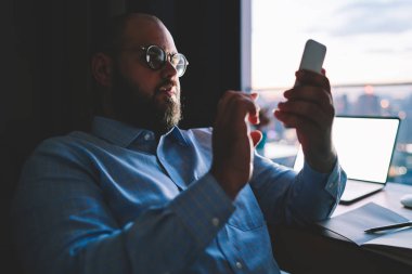 Ciddi erkek Smartphone online ödeme akşam, işadamı masaüstü tarama web sitesinde bankacılık App teyit Smartphone cep telefonu ile serbest evde çalışma hakkında bildirim okunurken holding