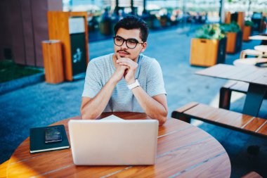 Şık gözlük modern dizüstü bilgisayar kablosuz yüksek hızlı 4 g ile öğrenim kurs için ilginç fikirler üzerinde düşünme düşünceli yakışıklı genç adam ahşap masada oturan internet