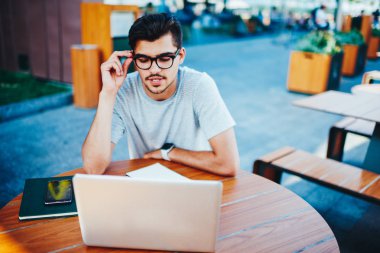 Ahşap açık havada terasta masadan modern dizüstü bilgisayar sınav öğrenim için hazırlanması ve internet sitelerinden bilgi okuma optik gözlükler dalgın yetenekli öğrenci