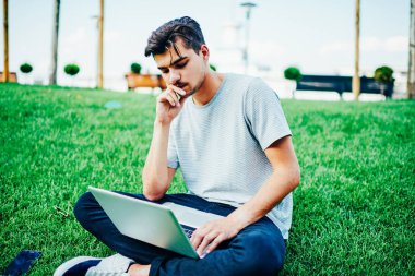 Netbook web sitelerinde bilgi okuma konsantre yetenekli öğrenci bağlı 4 g için Internet Üniversitesi topraklarında. Yeşil çimenlerin üzerinde oturan dizüstü eğitsel izlerken dalgın hipster blogger